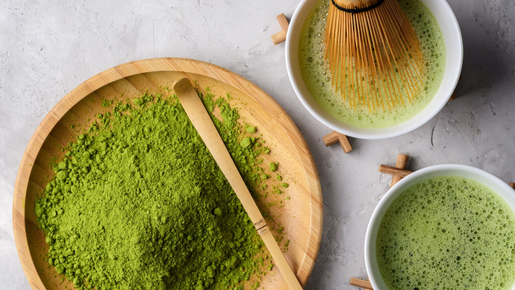 Matcha green tea, powder matcha on a wooden round plate,welded powder in white Tawan,tasaku and a bamboo whisk on white concrete background