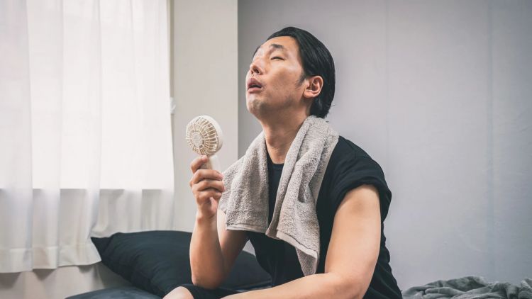 Ilustrasi. Seorang pria berusaha mendinginkan tubuh dengan kipas portable (Pakutaso).